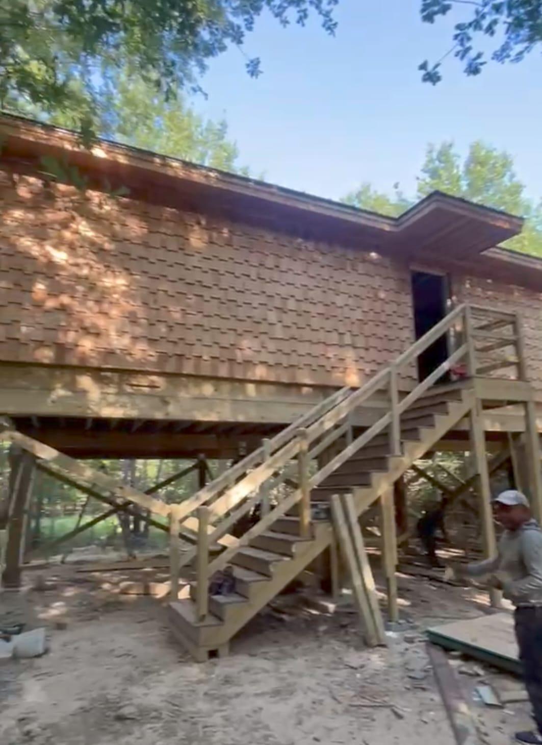 Wood-clad cabin under construction with timber stairs and an elevated deck.